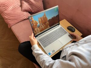 Osoba korzystająca z laptopa i myszki na ergonomicznej podstawce LapPad, siedząc na różowej kanapie.