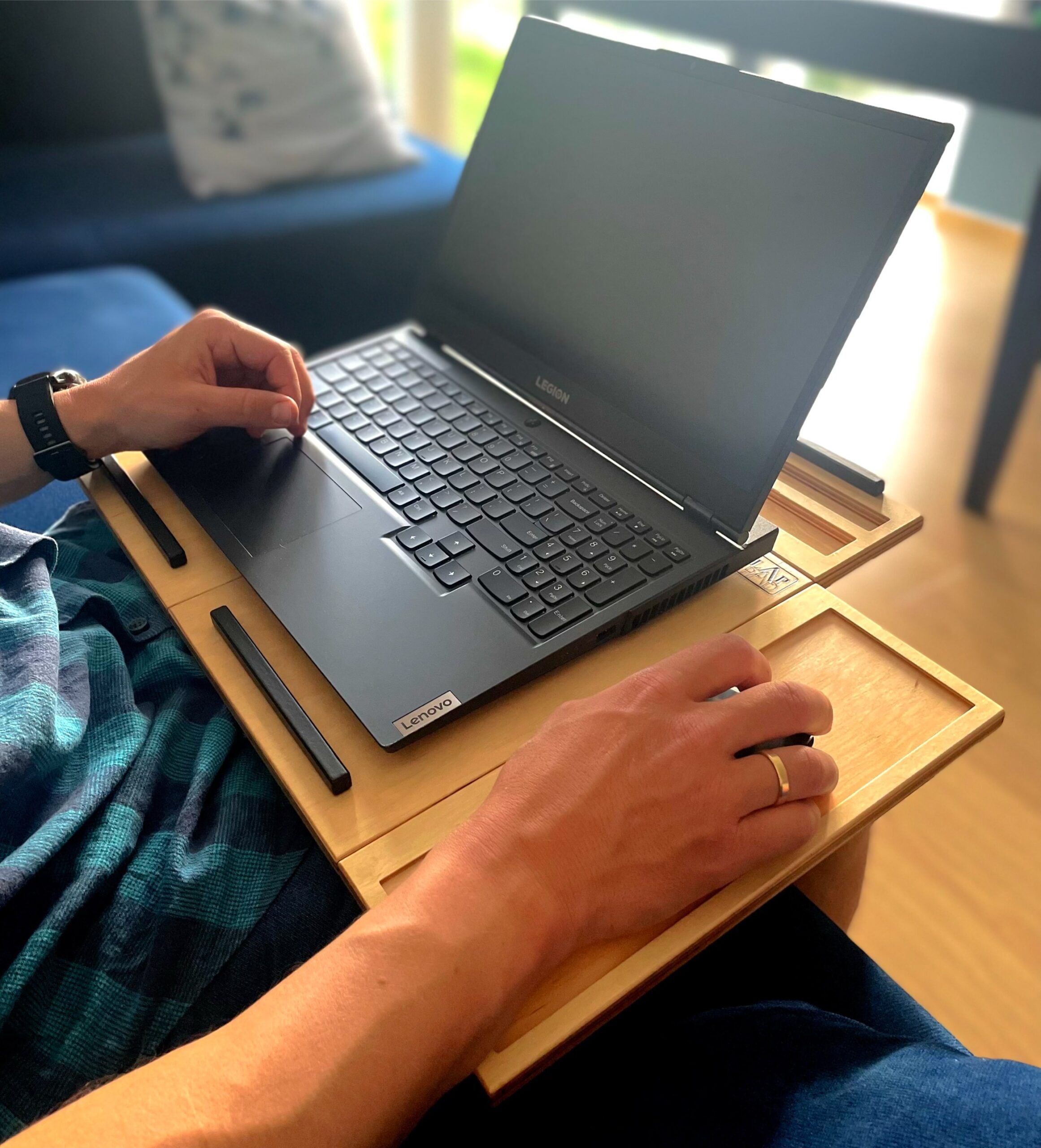 Osoba pracująca na laptopie Lenovo Legion przy użyciu podstawki LapPad, siedząc na kanapie.