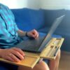 Osoba korzystająca z laptopa na podstawce LapPad w komfortowej pozycji, siedząc na niebieskiej kanapie.