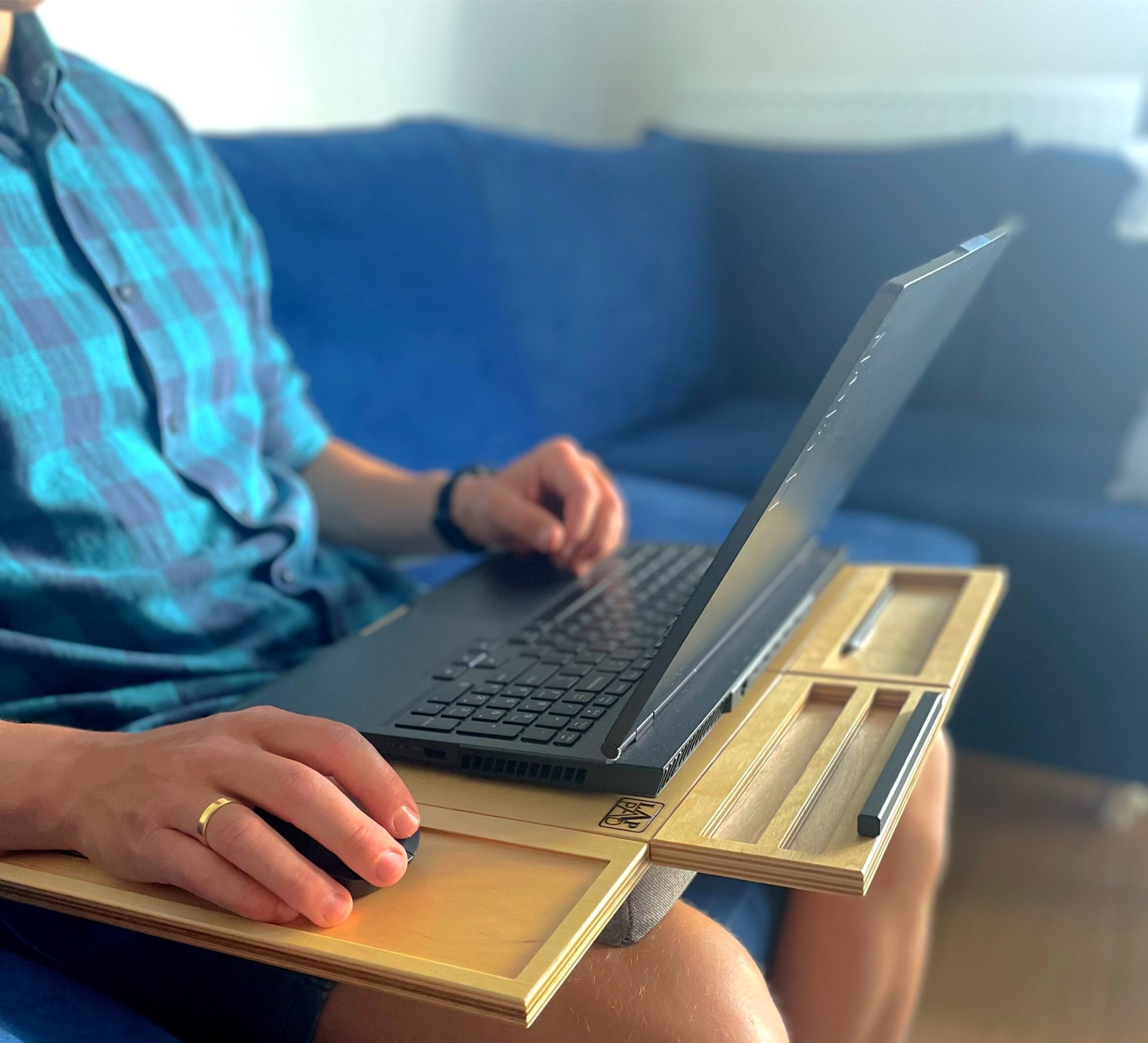 Osoba korzystająca z laptopa na podstawce LapPad w komfortowej pozycji, siedząc na niebieskiej kanapie.