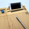 Moduł smartfon LapPad w naturalnym kolorze, zamontowany do podstawki pod laptopa, z uchwytem na smartfon, ołówkiem, długopisem i niebieskim kluczykiem montażowym, na białym tle.