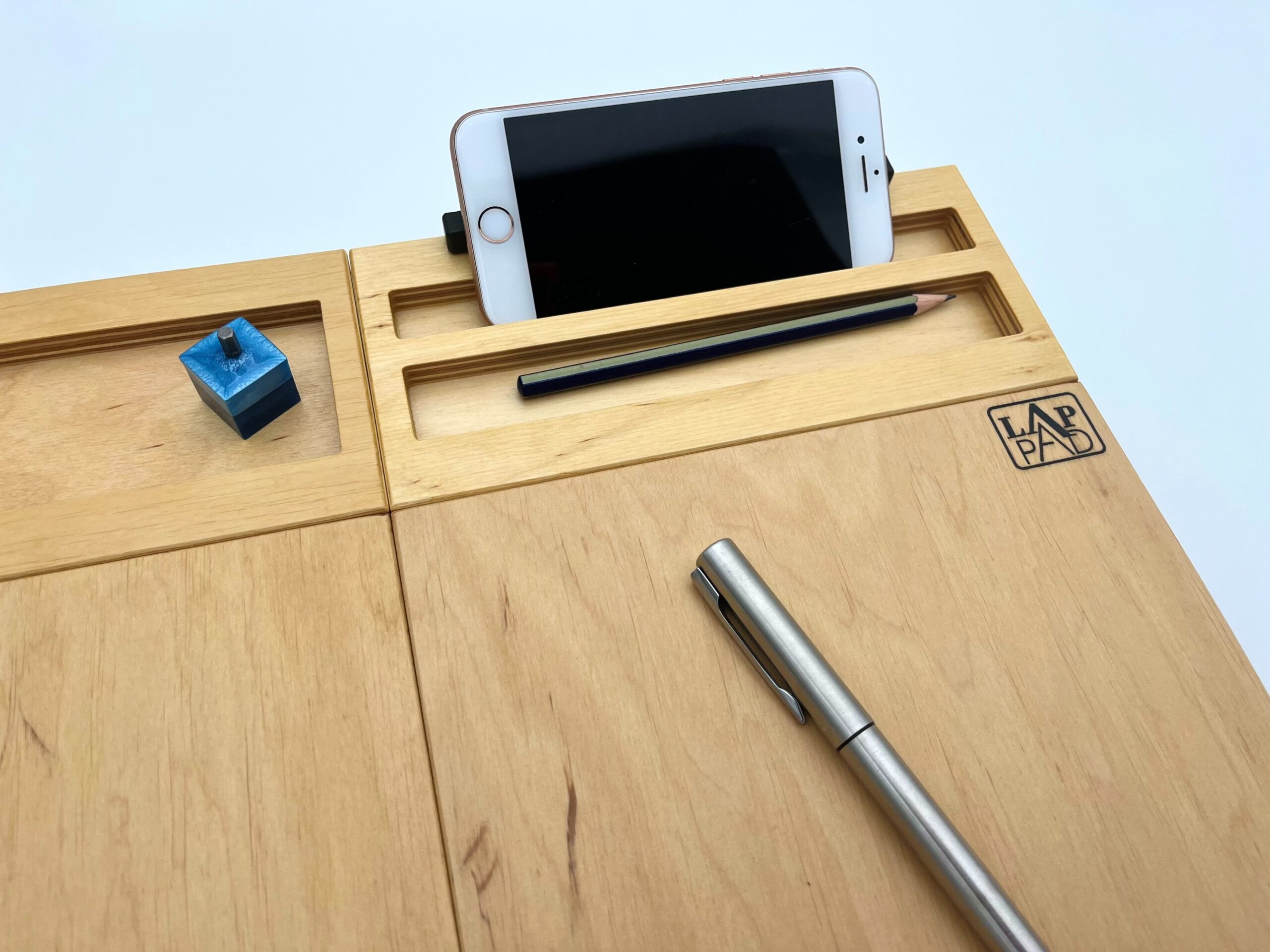 Moduł smartfon LapPad w naturalnym kolorze, zamontowany do podstawki pod laptopa, z uchwytem na smartfon, ołówkiem, długopisem i niebieskim kluczykiem montażowym, na białym tle.