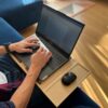 Mężczyzna pracujący na laptopie Lenovo z myszką, korzystający z ergonomicznej podstawki LapPad, siedząc na sofie w jasnym, nowoczesnym wnętrzu.